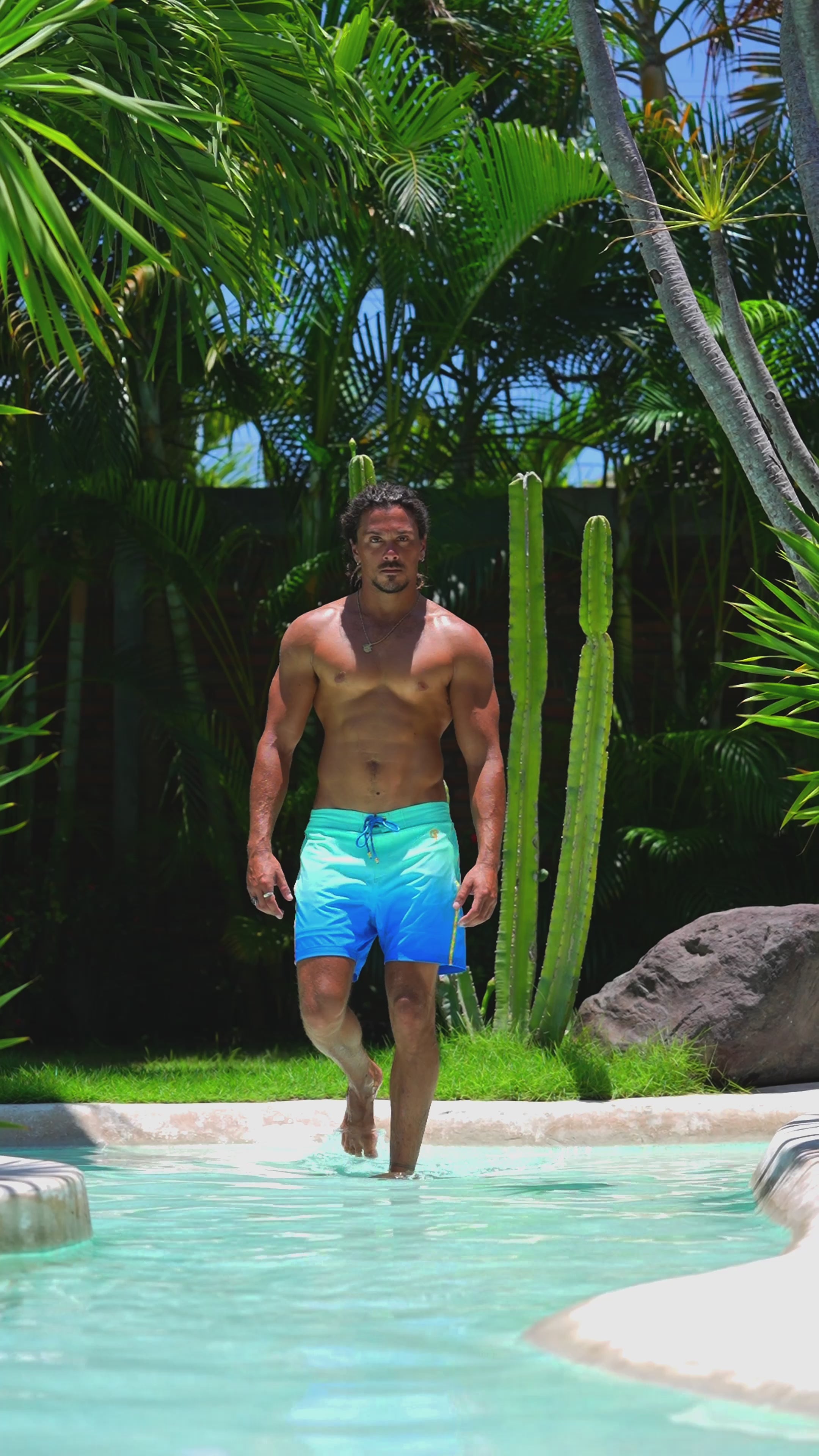 Man in faded ocean swim trunks near a tropical pool.
