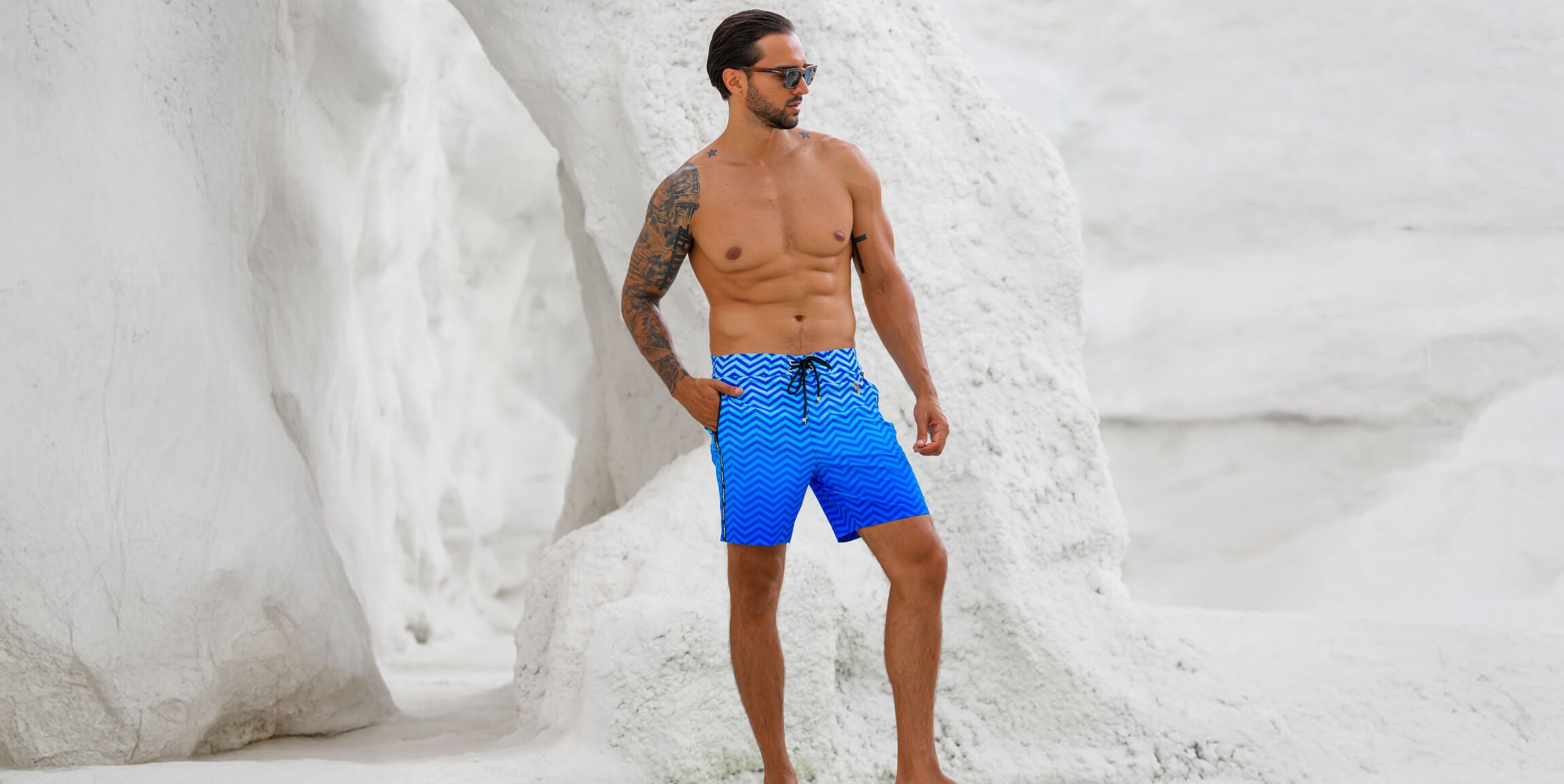Man wearing blue swim shorts with a pattern standing against a snowy background
