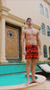 Man in orange swim shorts with a black palm tree design standing by a pool.