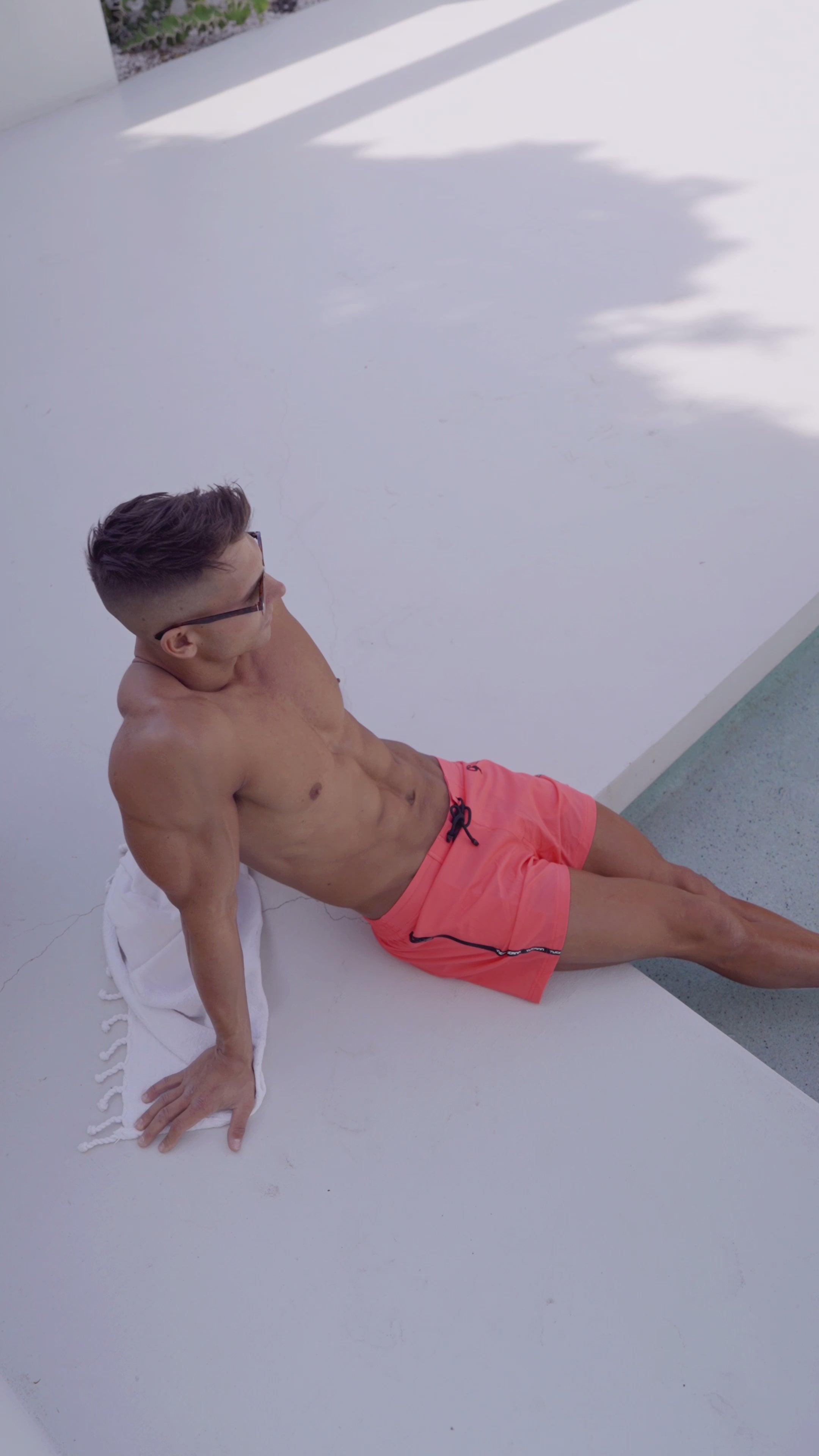 Man in watermelon colored swim trunk relaxing besides a pool