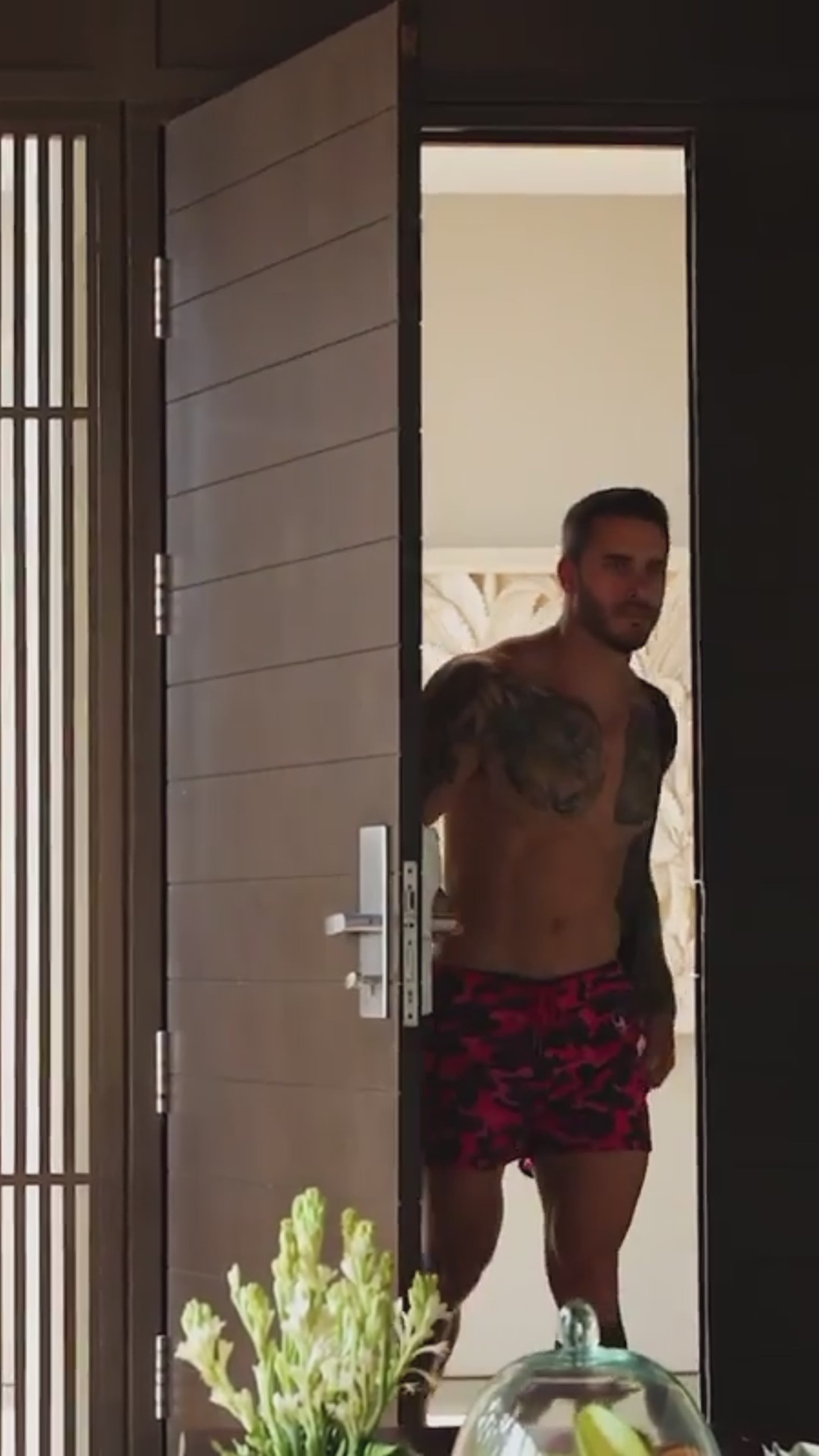 Man in pink camo swim shorts stepping out of a doorway.