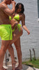 Man in neon yellow swim trunks and woman in a matching bikini standing under an outdoor shower.