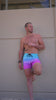 A man in blue-to-purple gradient swim trunks with a wave print design, posing by a wall.