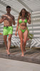 Couple walking by a poolside; man in lime green swim trunks, woman in a matching bikini.