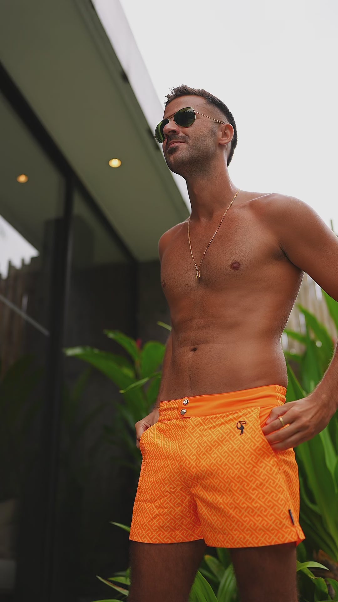 Man in tangerine swim trunks standing near a house