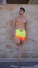 Man in sunset faded-waves swim trunks posing against a wall.