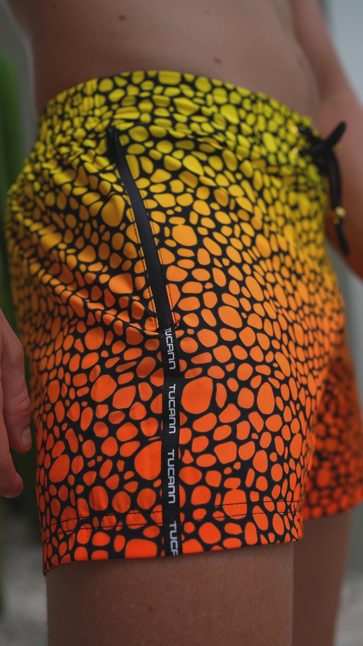 Close-up of a man in swim trunks with a sunset-inspired yellow to orange gradient pattern.