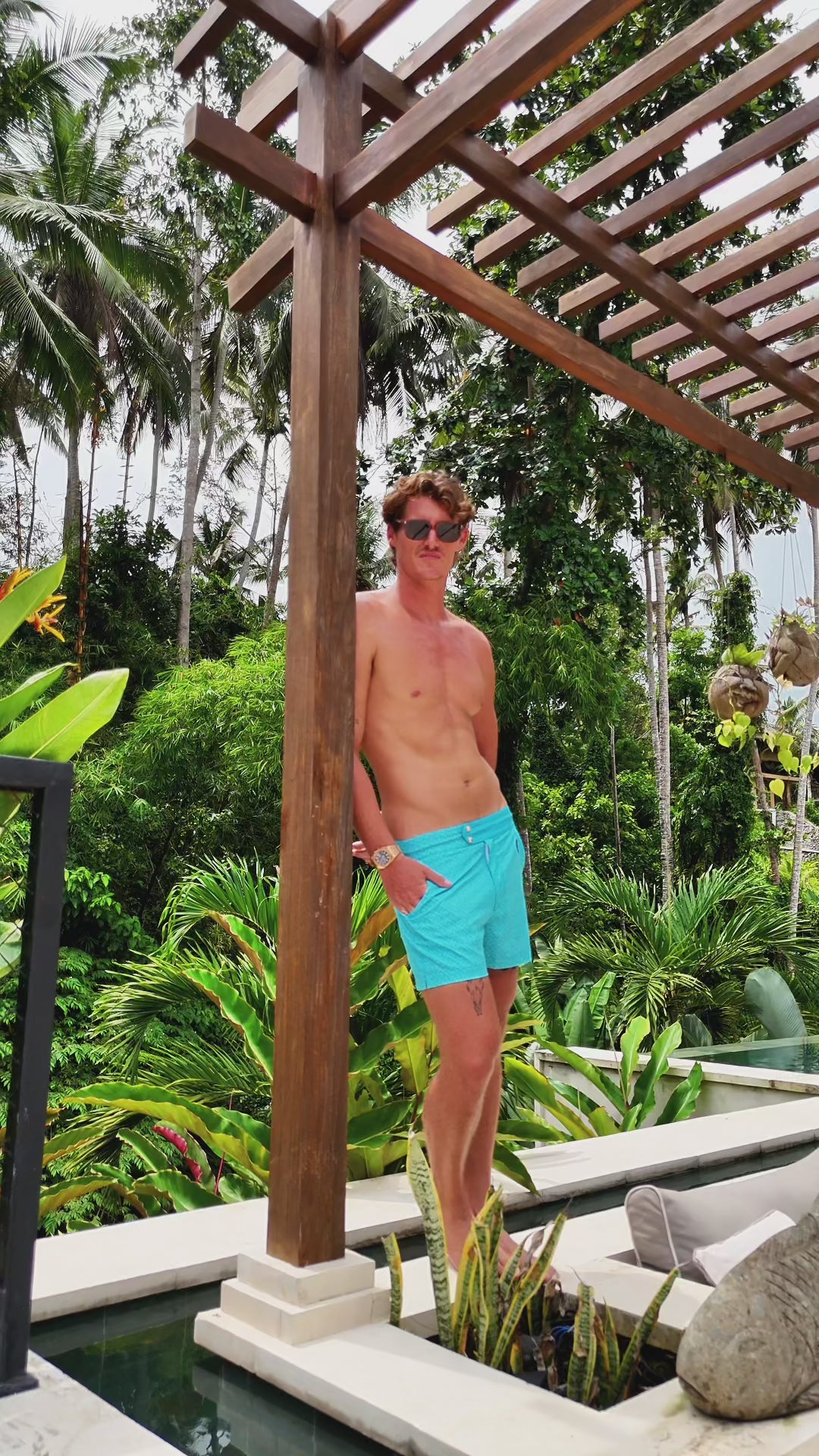 Man in aqua swim trunks standing by a pool.