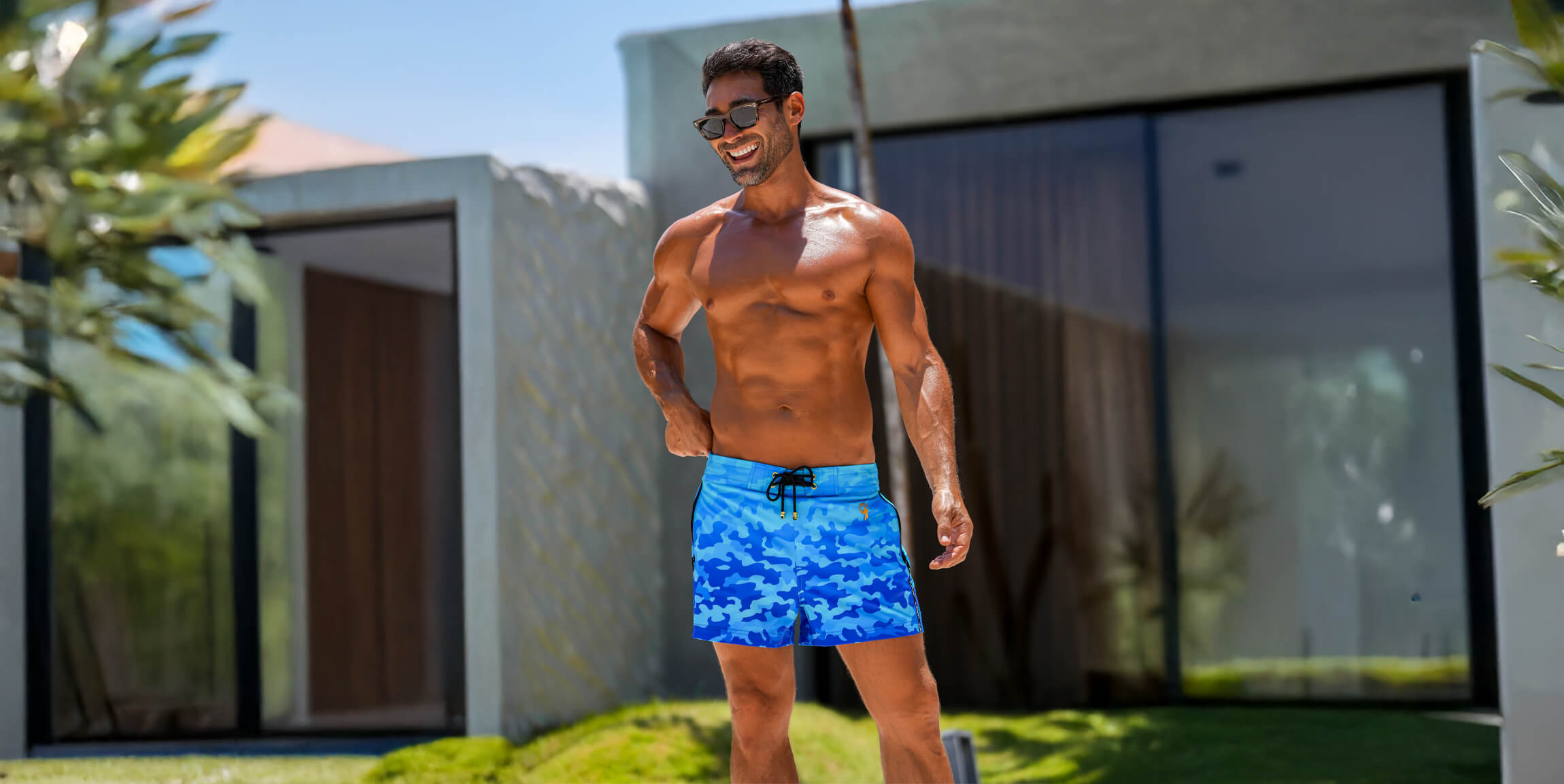Man wearing blue swim shorts standing outdoors with a modern building in the background